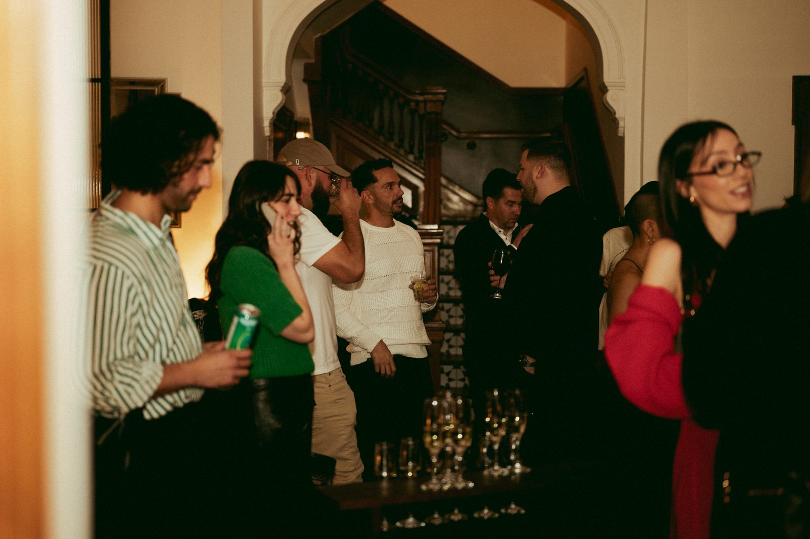 Guests with drinks gathered by the heritage staircase during a holiday party at Den 1880 in Uptown Waterloo