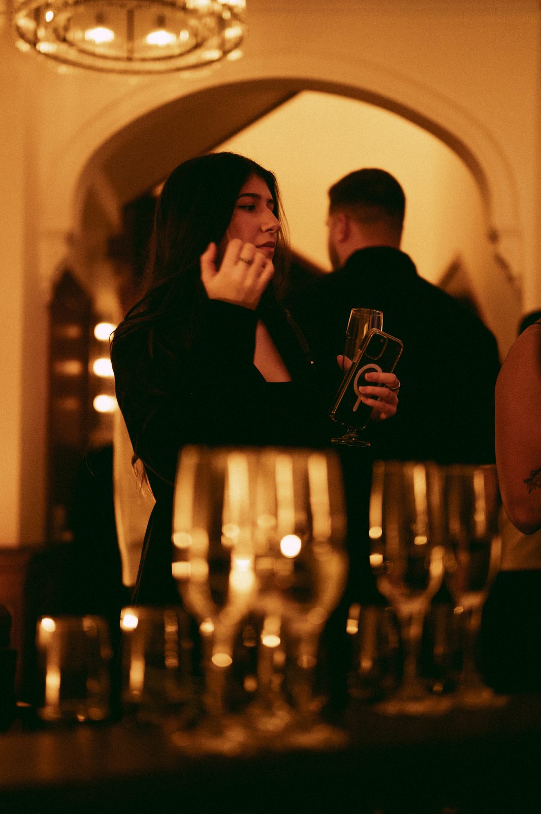 A guest holding a champagne flute behind rows of candlelit glassware at a Den 1880 holiday party