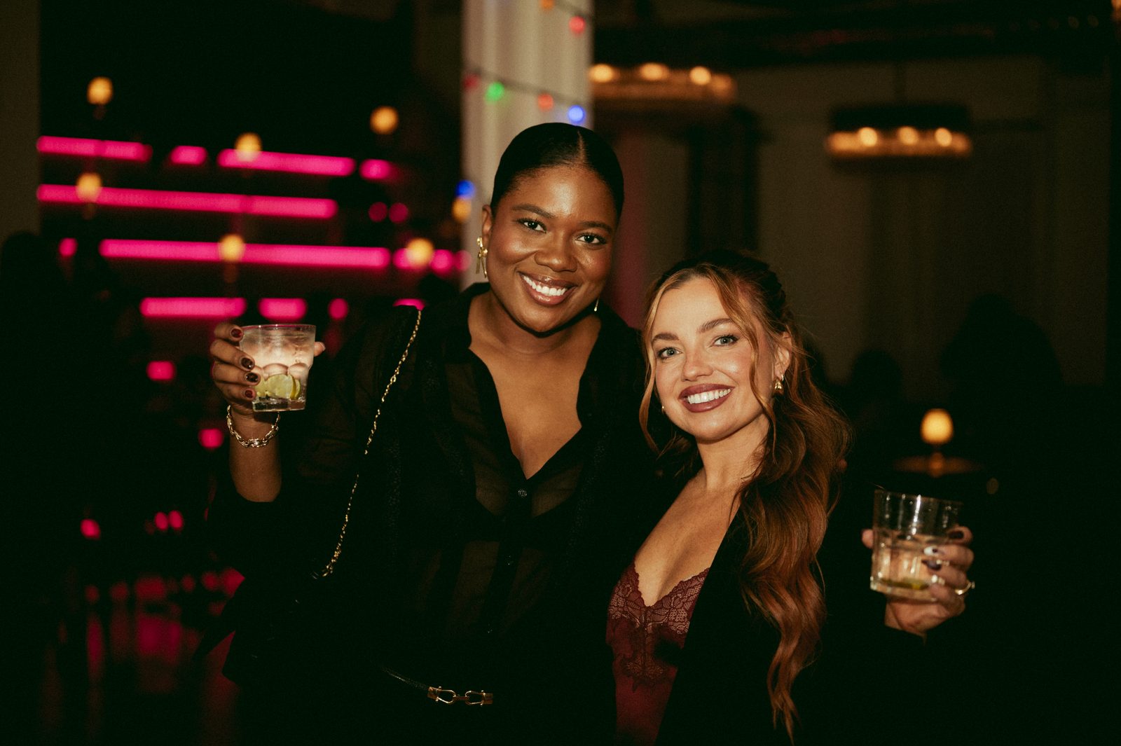 Two guests raising their drinks in front of neon lighting at a Den 1880 corporate holiday party