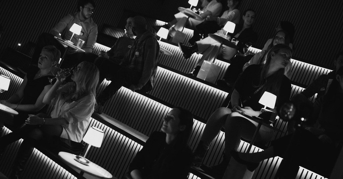 Guests seated with drinks at the tiered theatre seating inside Den 1880
