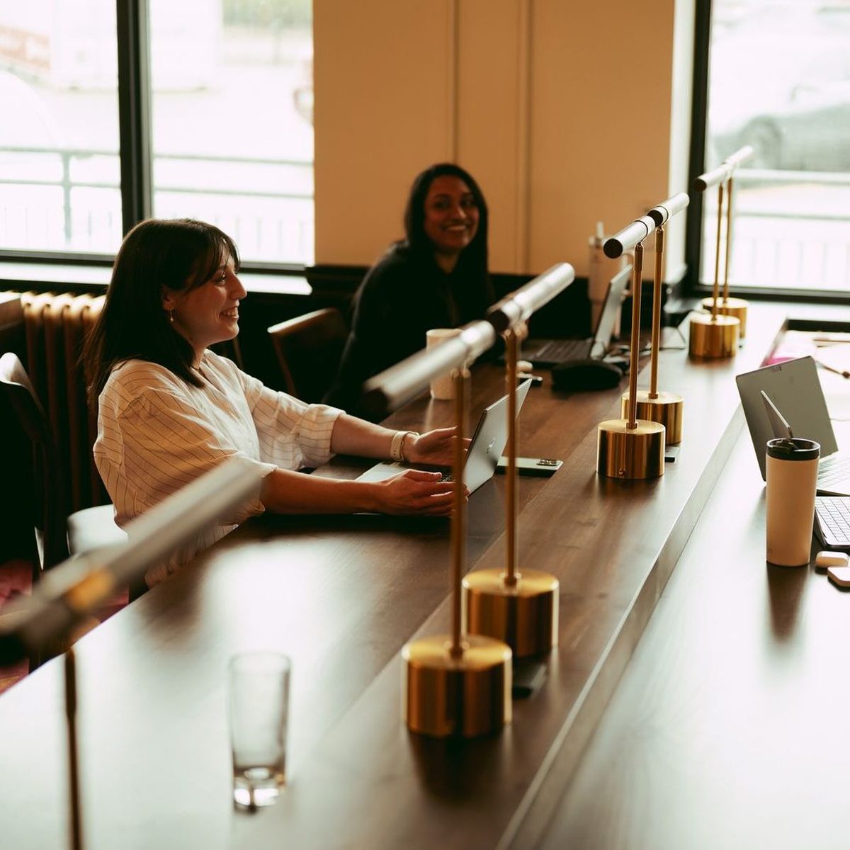 Two members working at the brass-lamped communal table on the coworking floor at Den 1880