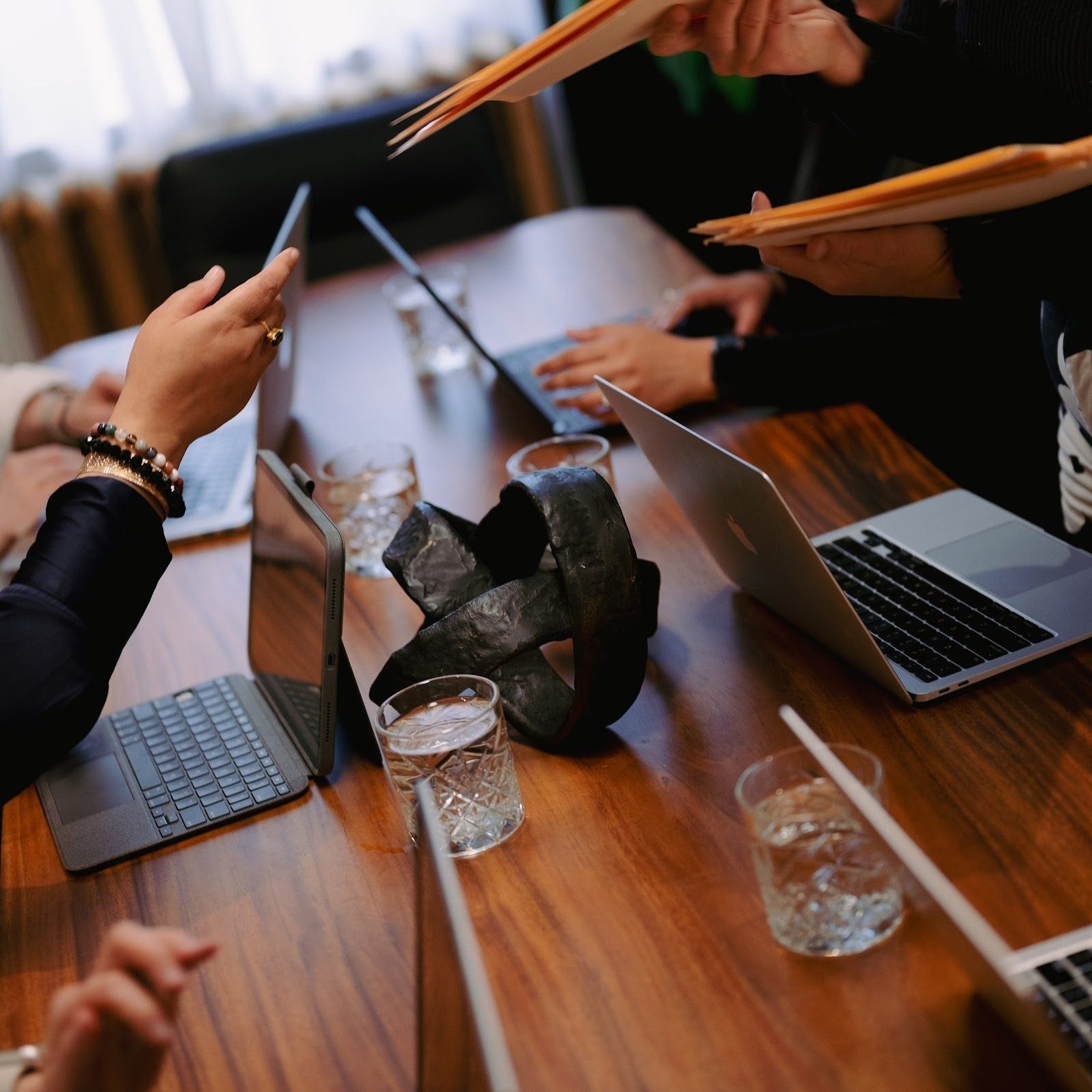 Laptops, a tablet and folders spread across the walnut boardroom table during a working session at Den 1880