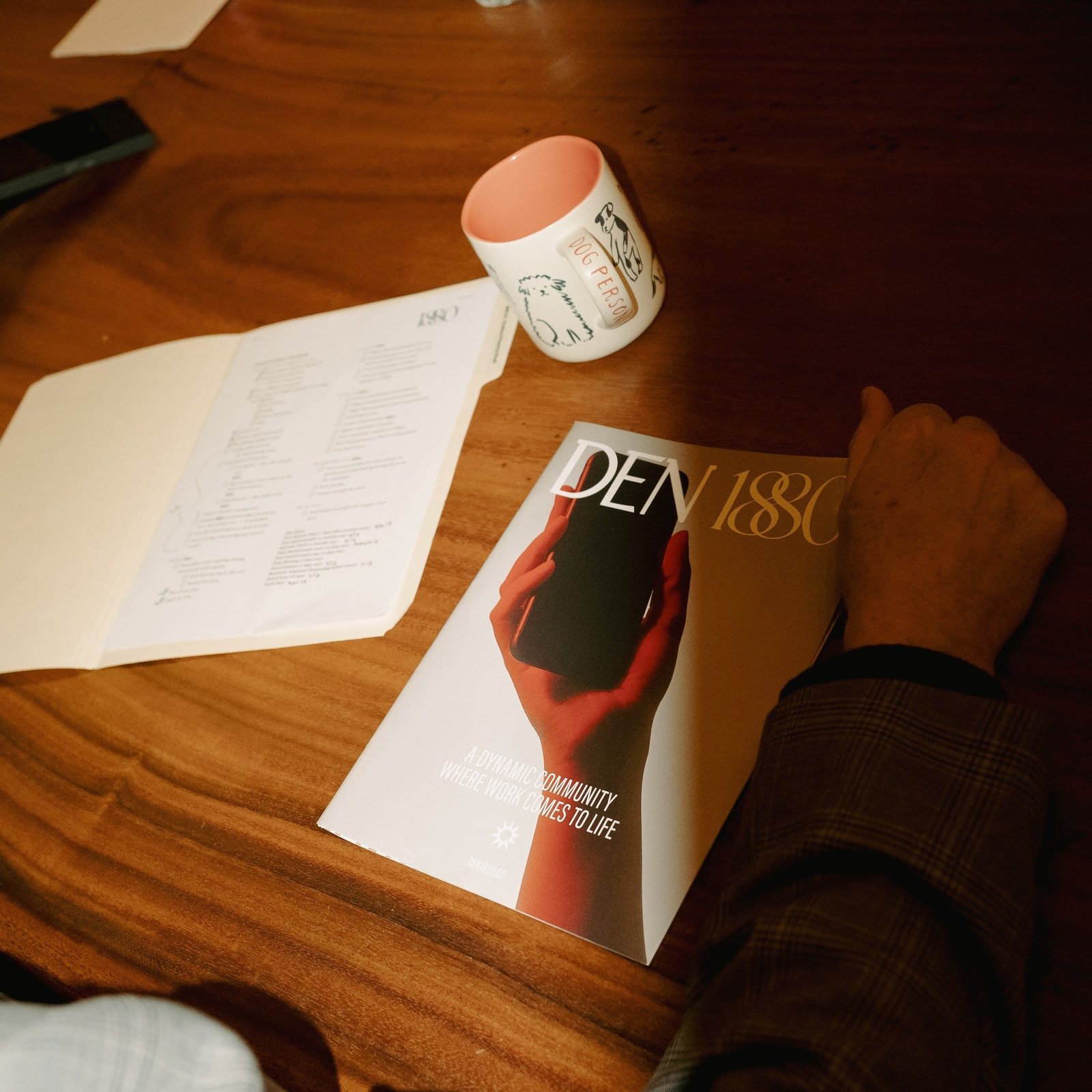 A Den 1880 magazine and meeting notes open on the table beside a coffee mug