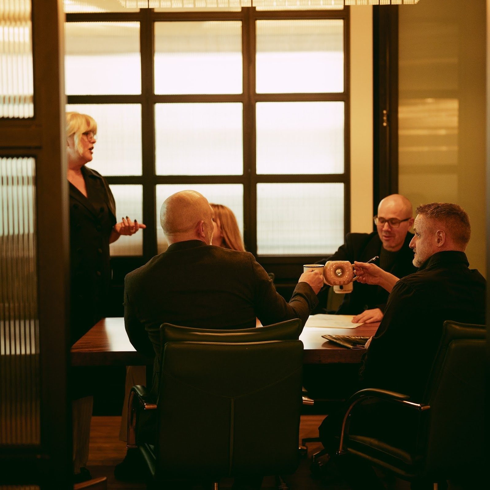 A meeting in progress seen through the fluted glass partition of a Den 1880 boardroom