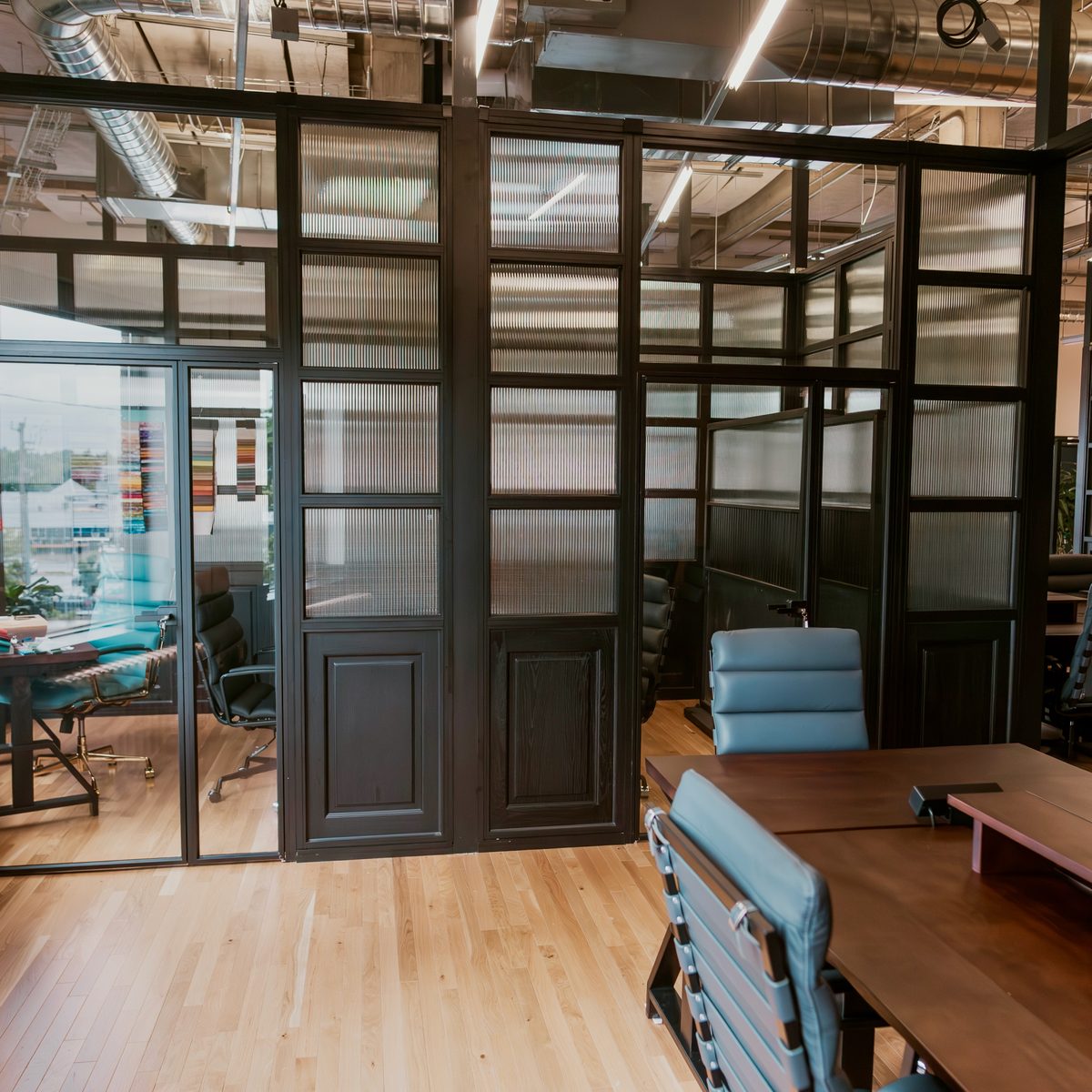 A private office suite at Den 1880 with a solid wood door set into a black-framed glass wall, a walnut desk and leather chairs