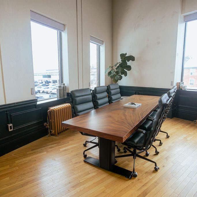 A daylit corner suite at Den 1880 with a live-edge table, heritage windows and a cast-iron radiator