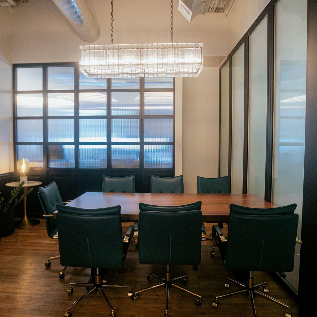 A team suite at Den 1880 with a meeting table, six green leather chairs and a brass chandelier