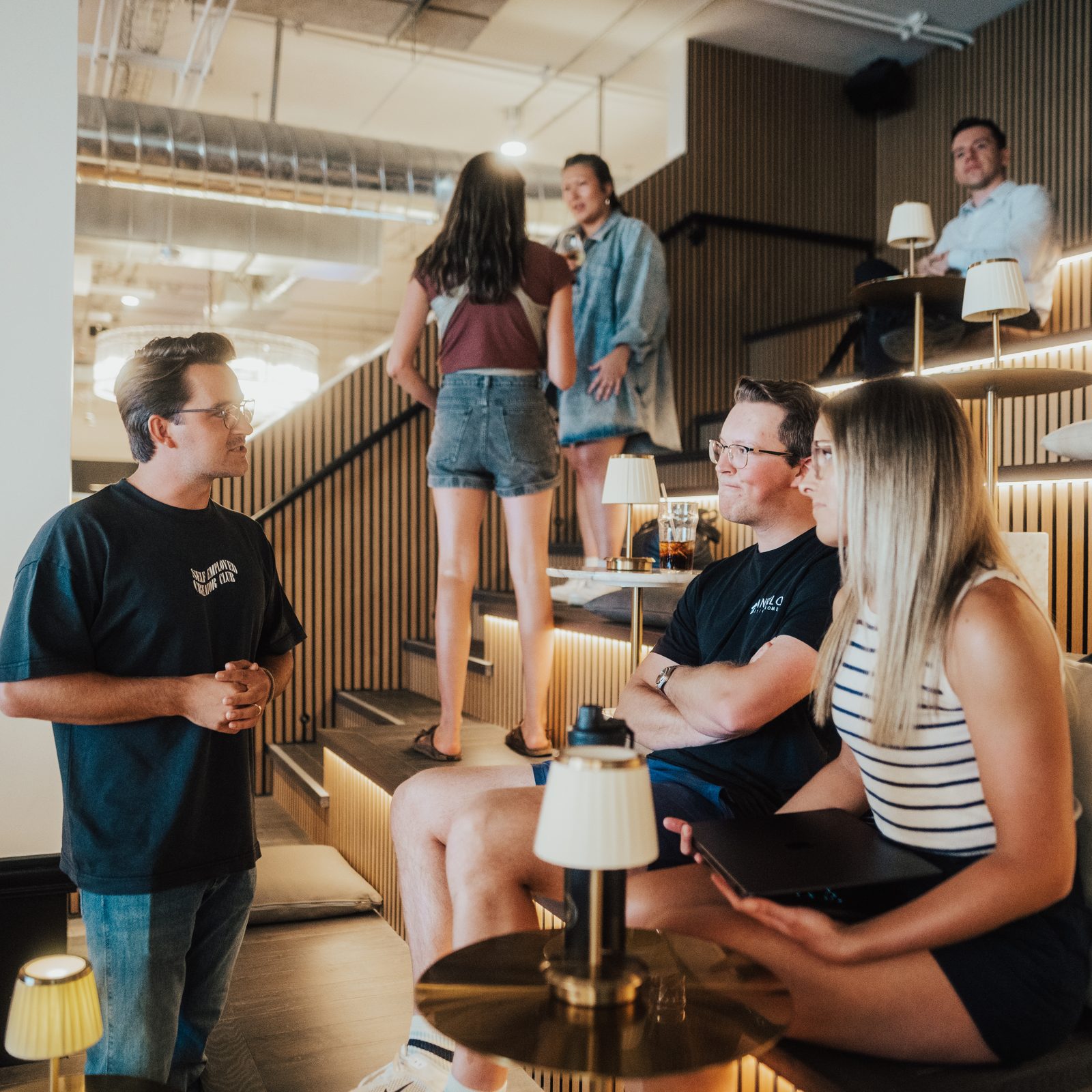 Coworkers talking on the tiered lounge seating during a break in a team offsite at Den 1880