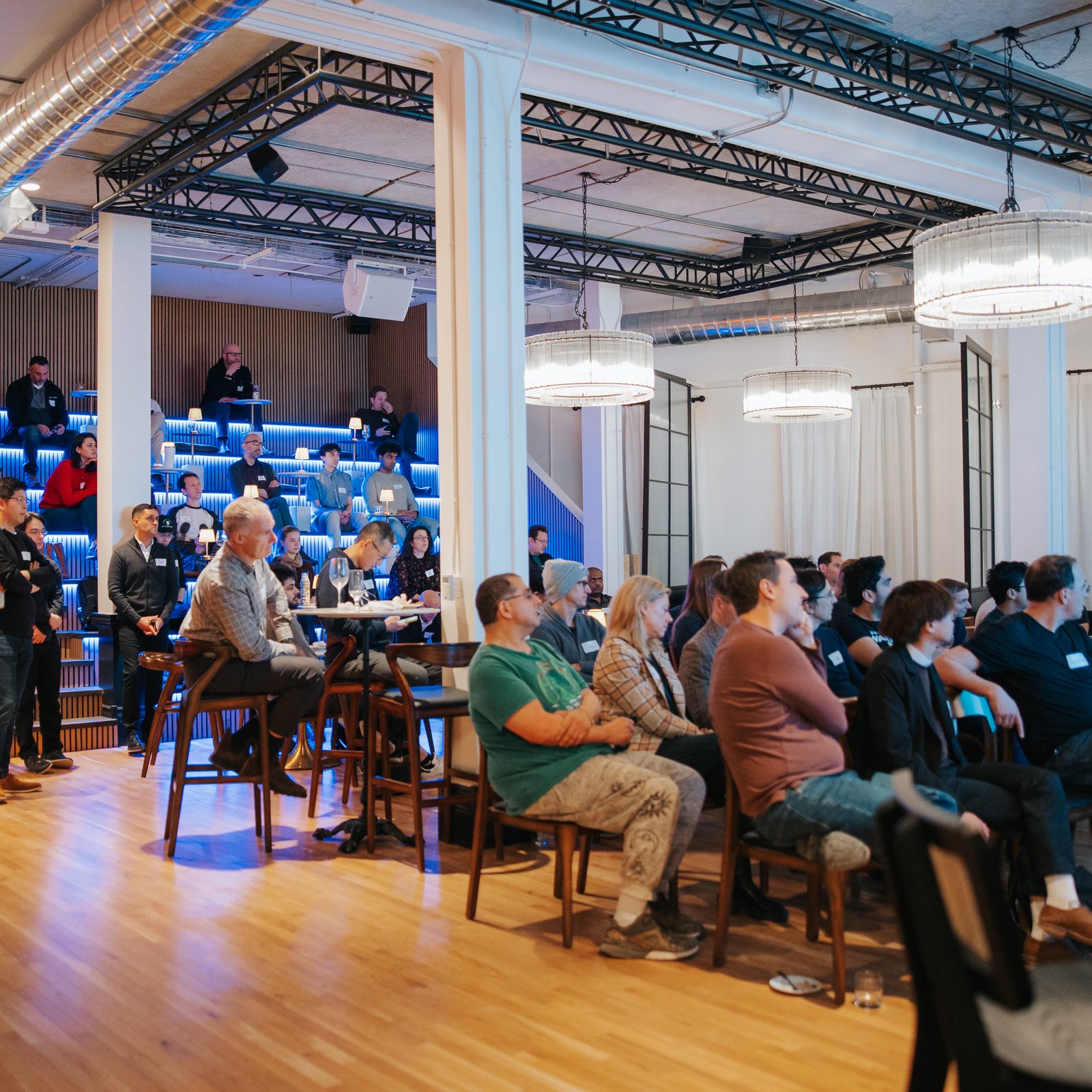 A full company audience seated on the tiered theatre seating for an all-hands session at Den 1880