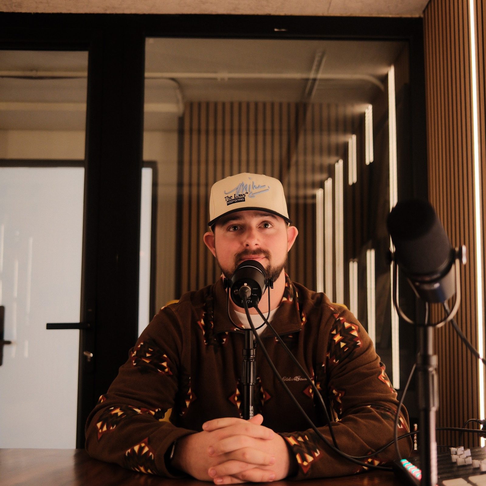 A host seated at the recording table in The Vault, headphones round his neck and a microphone in front of him