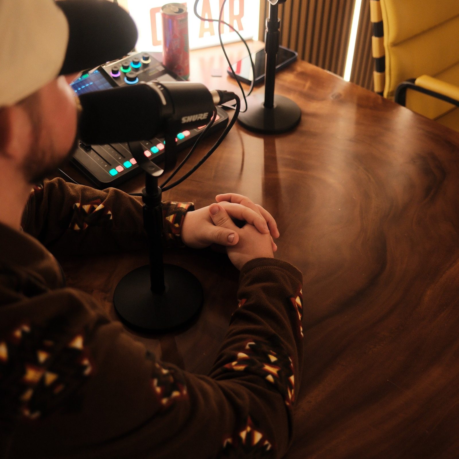 Close view over a host's shoulder showing his hands resting on the walnut recording desk beside the mixer