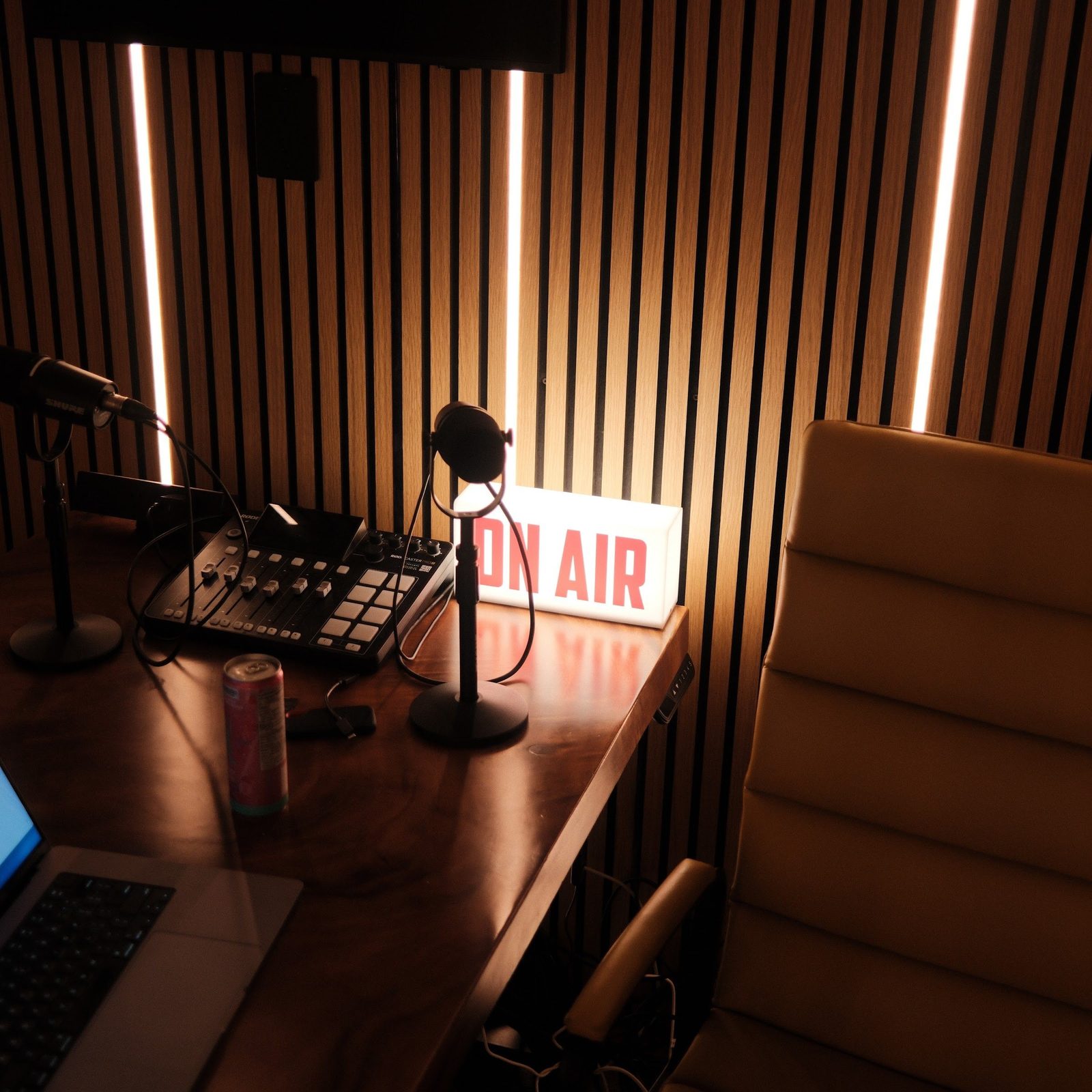 The lit ON AIR sign on the recording desk next to the mixer, microphone and a laptop
