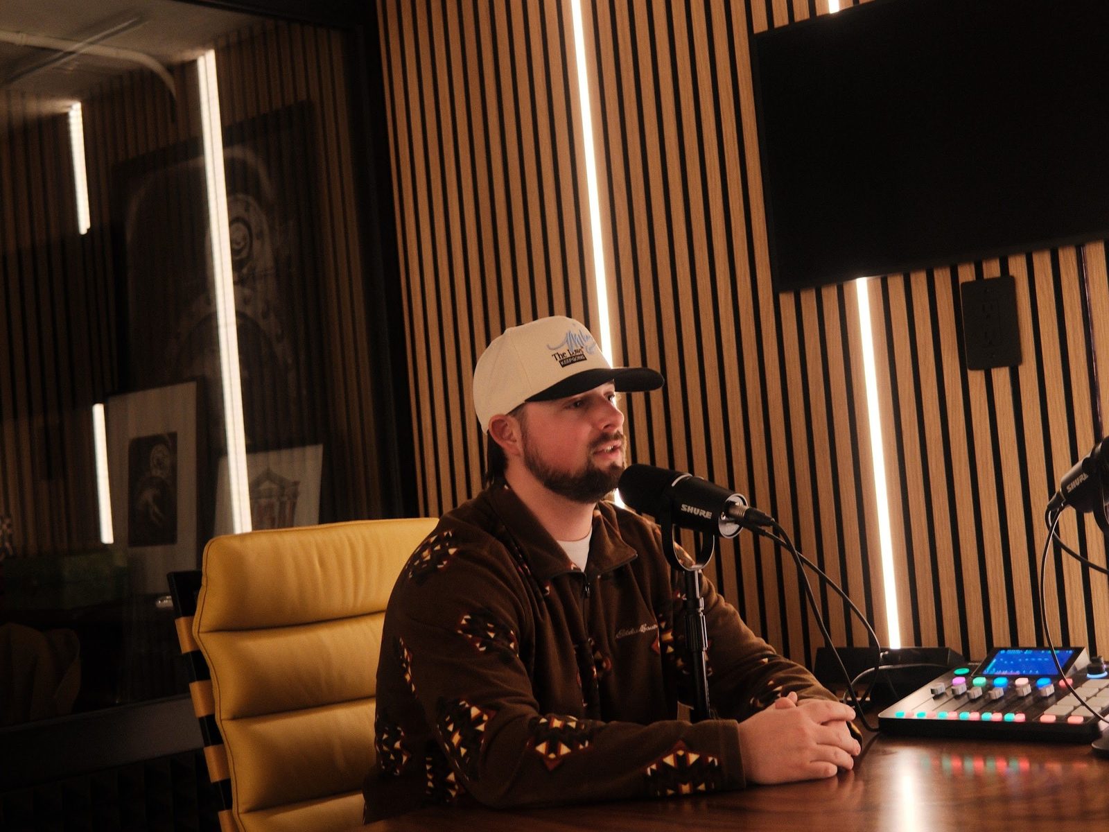 A host speaking into a Shure microphone at the recording table inside The Vault at Den 1880